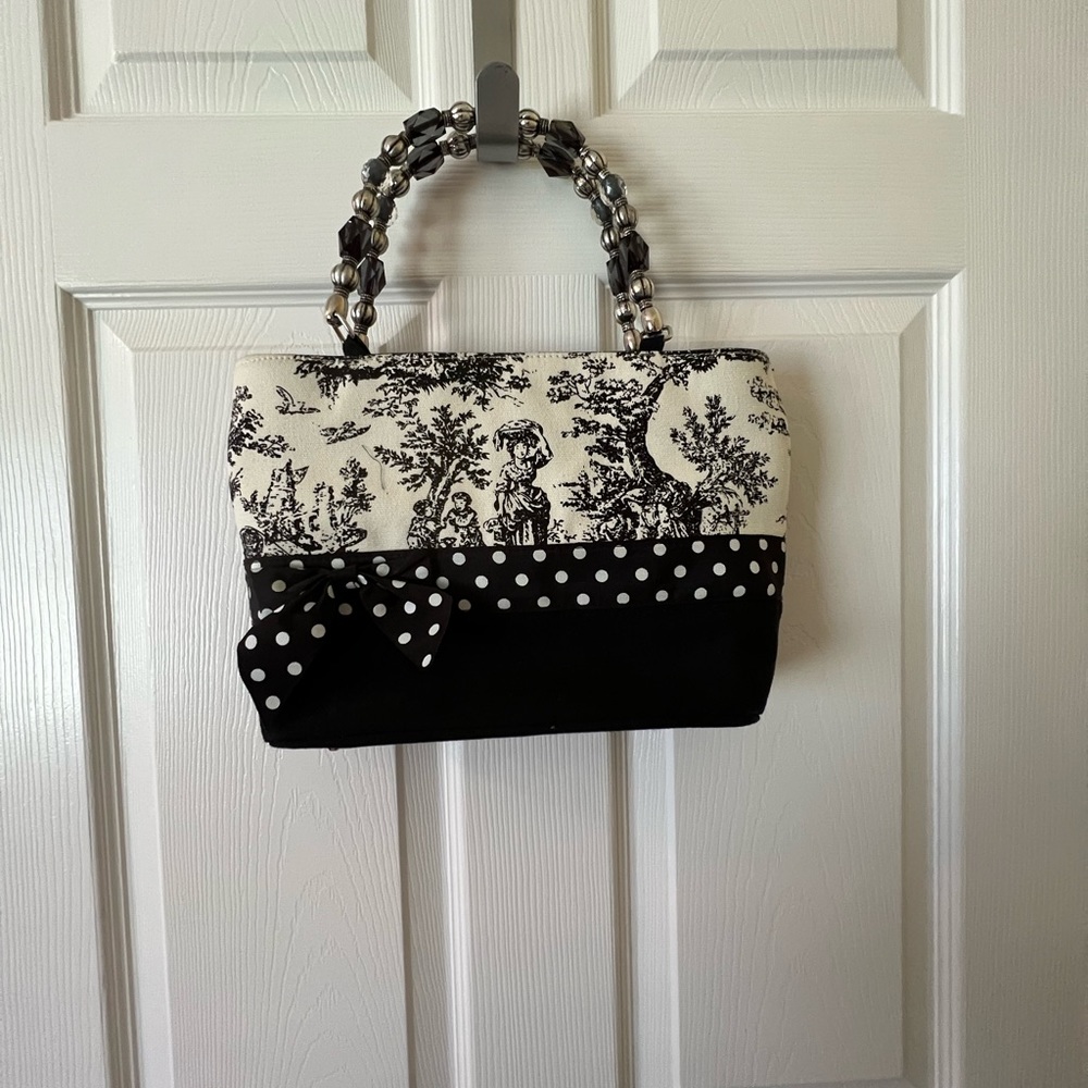 Beaded handles handbag. Inside one zipper pocket, elastic pocket and flat one.
